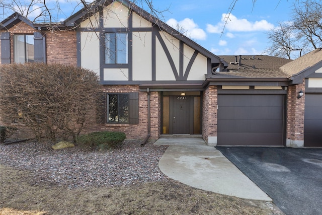 tudor-style house with brick siding, stucco siding, aphalt driveway, and a garage