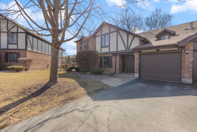 english style home featuring brick siding, a front lawn, aphalt driveway, stucco siding, and a garage