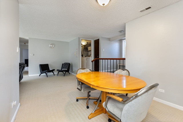 dining space featuring baseboards, visible vents, washing machine and clothes dryer, a textured ceiling, and light colored carpet