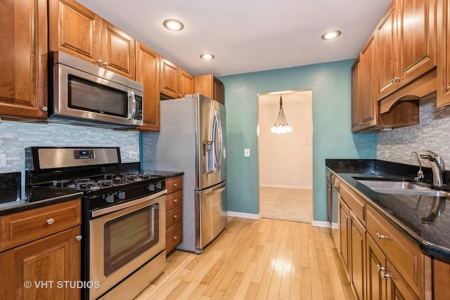 kitchen featuring light wood-type flooring, a sink, appliances with stainless steel finishes, an inviting chandelier, and baseboards