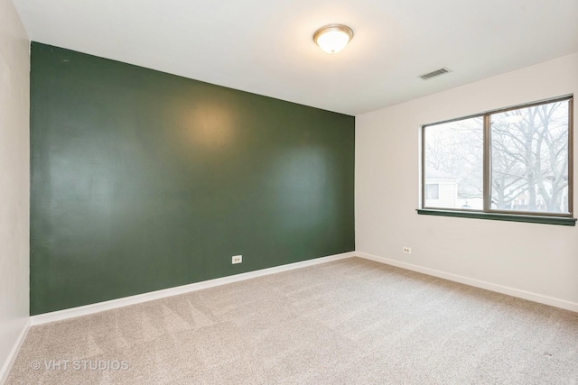 empty room featuring visible vents, baseboards, an accent wall, and carpet flooring