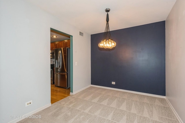 spare room featuring an inviting chandelier, light colored carpet, visible vents, and baseboards