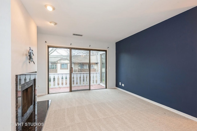 unfurnished living room featuring a high end fireplace, carpet flooring, visible vents, and baseboards