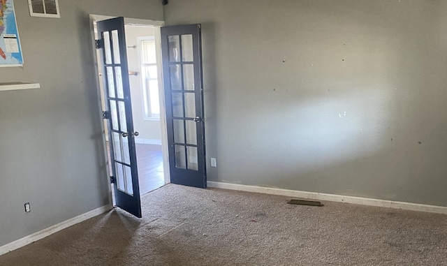 carpeted empty room with french doors, visible vents, and baseboards