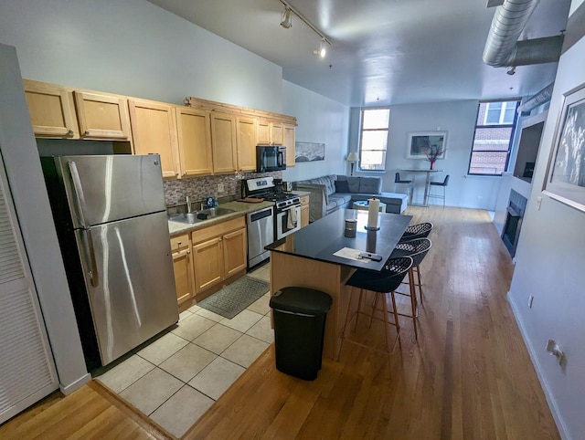 kitchen featuring backsplash, a kitchen island, light brown cabinetry, appliances with stainless steel finishes, and a sink