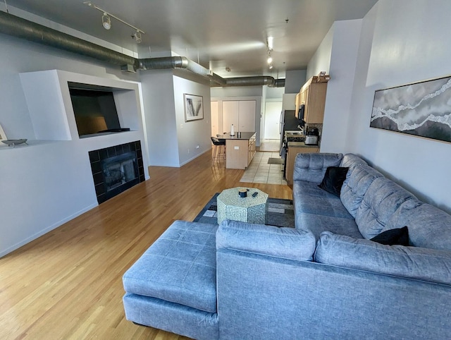 living room with rail lighting, a fireplace, baseboards, and light wood finished floors