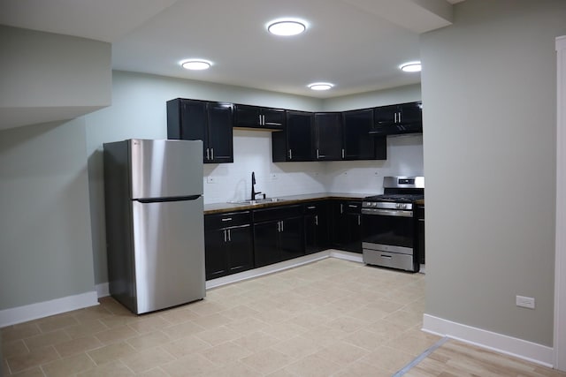 kitchen with baseboards, decorative backsplash, appliances with stainless steel finishes, dark cabinetry, and a sink