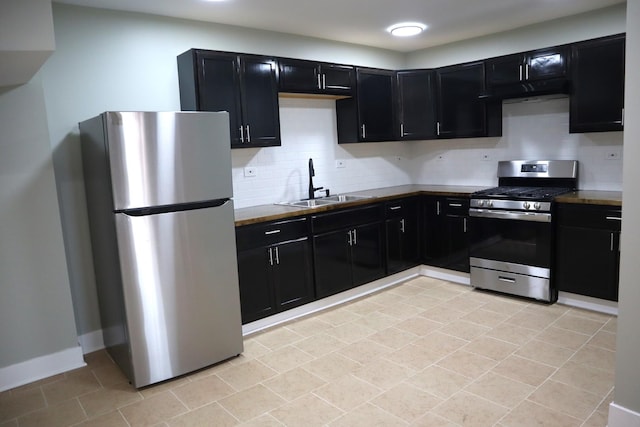 kitchen with baseboards, decorative backsplash, appliances with stainless steel finishes, dark cabinetry, and a sink