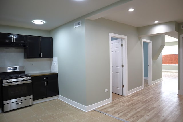 kitchen featuring visible vents, baseboards, stainless steel range with gas stovetop, decorative backsplash, and dark cabinets