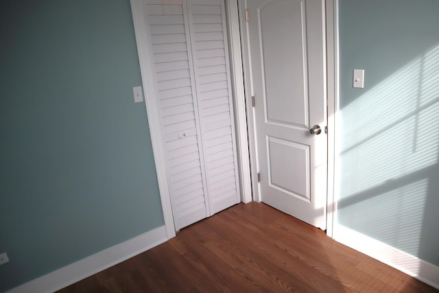 unfurnished bedroom featuring dark wood-style floors, baseboards, and a closet