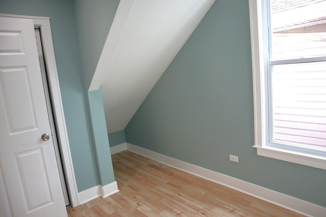 additional living space with lofted ceiling, a healthy amount of sunlight, baseboards, and light wood-type flooring