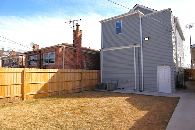 rear view of house featuring central AC unit, fence, and a lawn