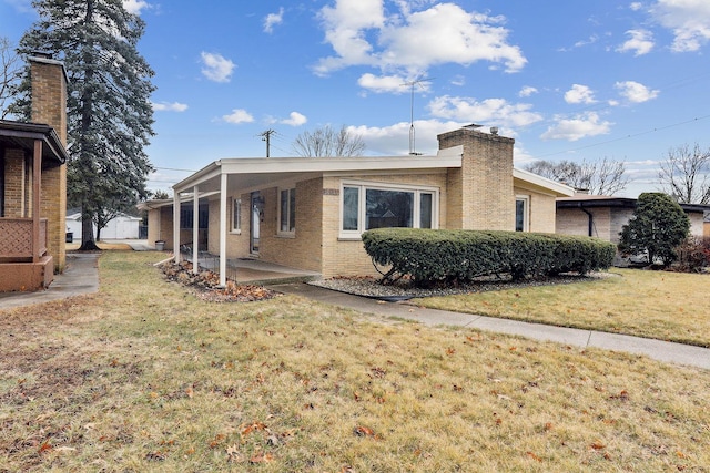 view of side of home with brick siding, an attached carport, a lawn, a chimney, and a patio