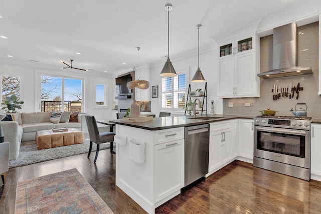 kitchen featuring a sink, dark countertops, stainless steel appliances, open floor plan, and wall chimney exhaust hood