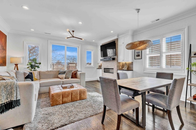 dining area with a glass covered fireplace, plenty of natural light, ornamental molding, and dark wood finished floors