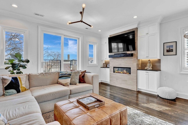 living area with crown molding, visible vents, a wealth of natural light, and dark wood-type flooring