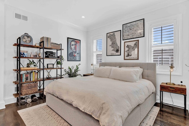bedroom with wood finished floors, visible vents, crown molding, and baseboards