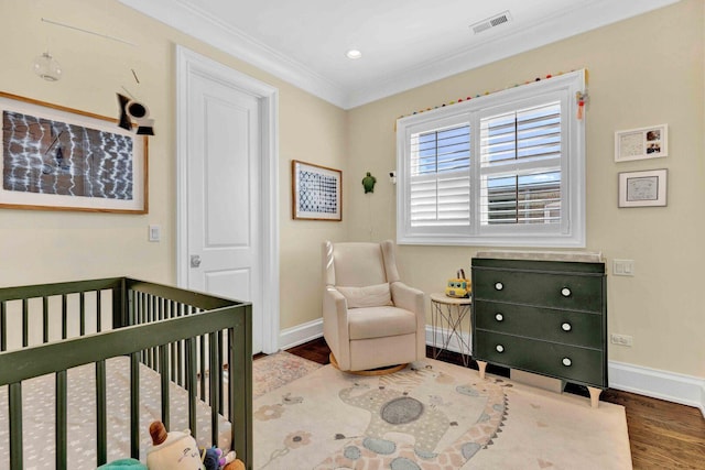 bedroom with crown molding, visible vents, baseboards, a crib, and wood finished floors