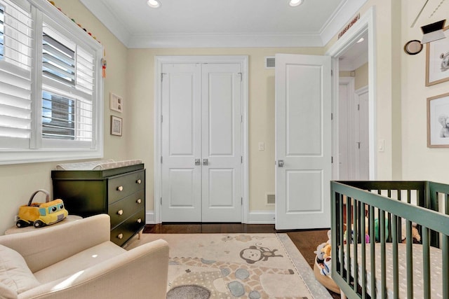 bedroom with recessed lighting, a nursery area, a closet, ornamental molding, and dark wood-style floors