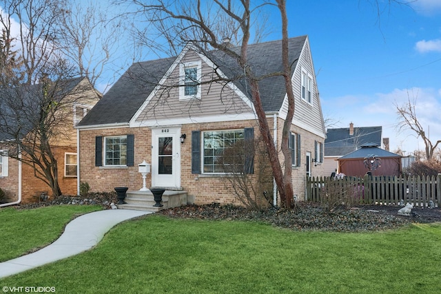 view of front of property with brick siding, roof with shingles, a front lawn, and fence