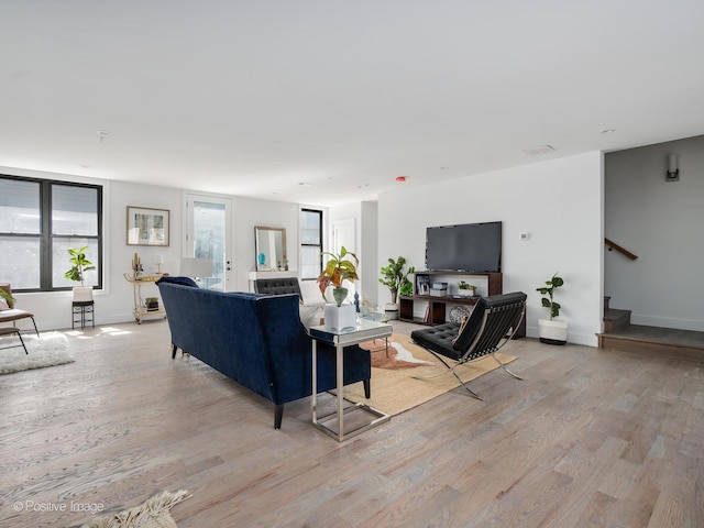 living room featuring light wood-type flooring, baseboards, and stairway