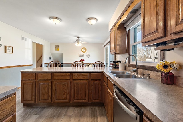 kitchen with a ceiling fan, a sink, stainless steel dishwasher, wood finished floors, and a peninsula