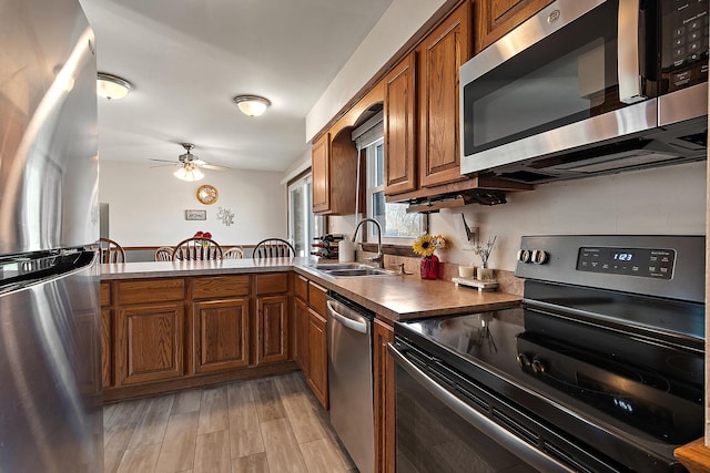 kitchen with brown cabinets, appliances with stainless steel finishes, light wood-style flooring, a ceiling fan, and a sink