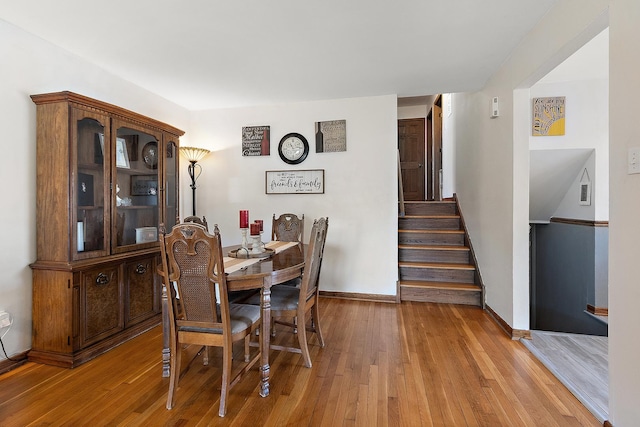 dining space with light wood-type flooring, baseboards, and stairway