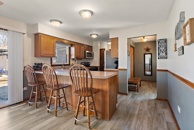 kitchen featuring a kitchen bar, a peninsula, light wood finished floors, and appliances with stainless steel finishes