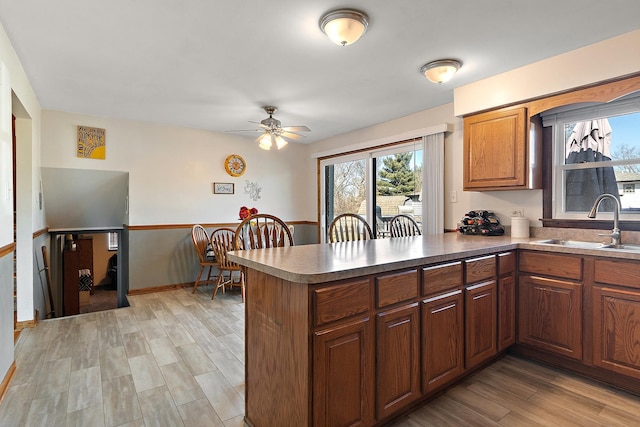 kitchen with light wood-type flooring, brown cabinets, a sink, a peninsula, and ceiling fan