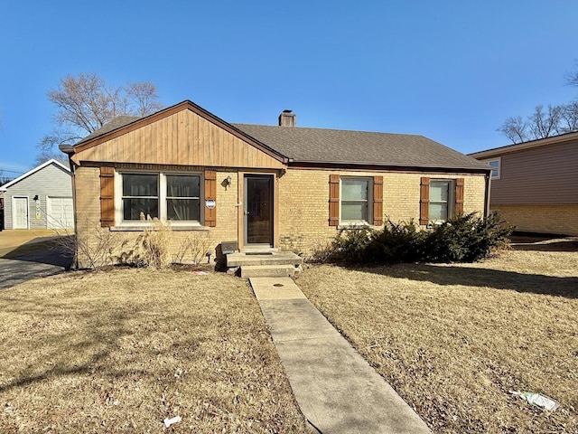 view of front of house featuring brick siding, a chimney, roof with shingles, an outdoor structure, and a front lawn