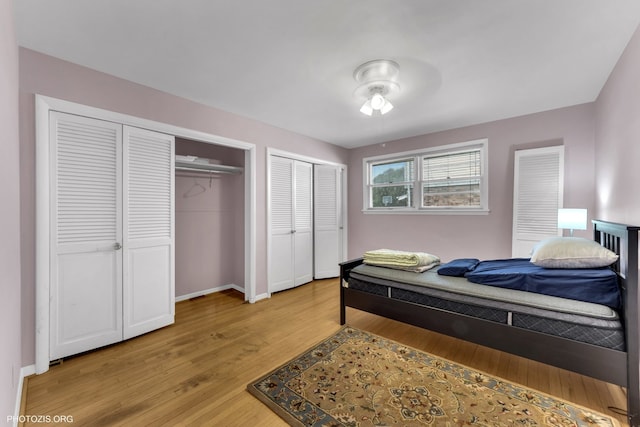 bedroom with light wood finished floors, baseboards, and two closets