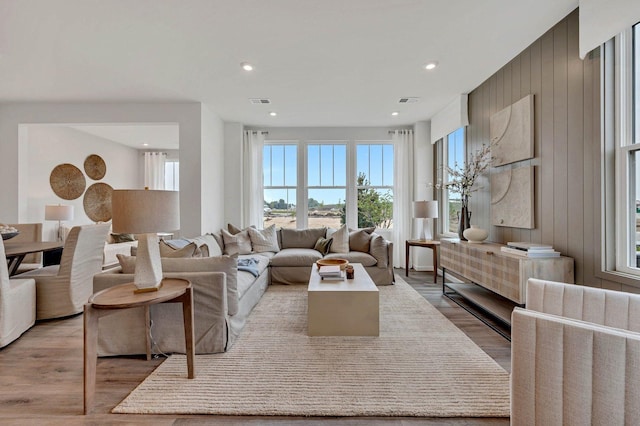 living room with light wood finished floors, wooden walls, recessed lighting, and visible vents