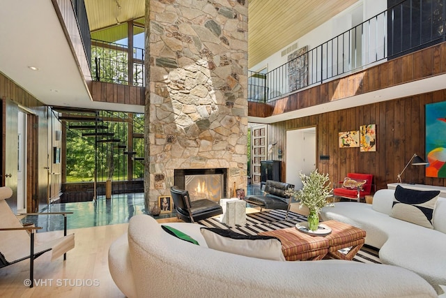 living area featuring a high ceiling, wood walls, a stone fireplace, and wood finished floors
