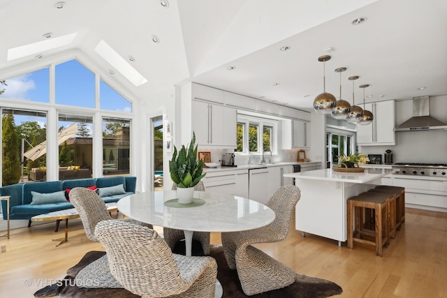 kitchen with wall chimney range hood, stainless steel gas cooktop, light countertops, a kitchen island, and a skylight