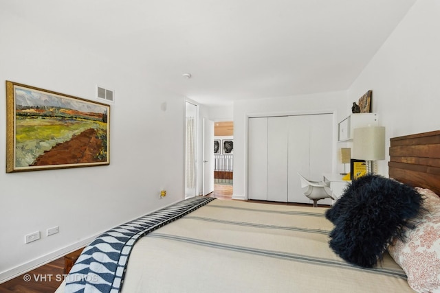 bedroom with a closet, baseboards, wood finished floors, and visible vents