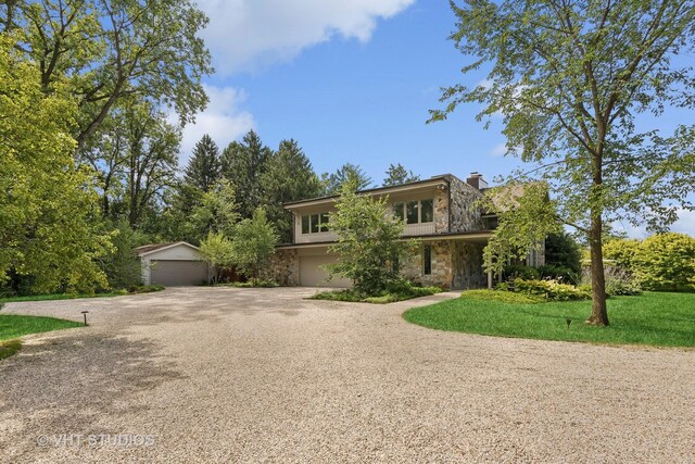 view of front facade with a chimney, gravel driveway, a front yard, and stone siding
