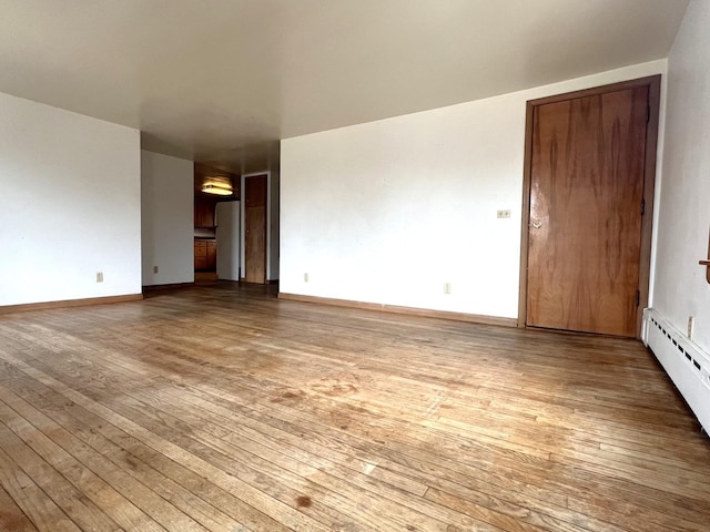 empty room featuring baseboards, wood-type flooring, and a baseboard radiator