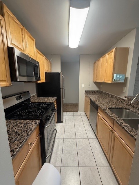 kitchen with light brown cabinets, dark stone counters, light tile patterned floors, stainless steel appliances, and a sink