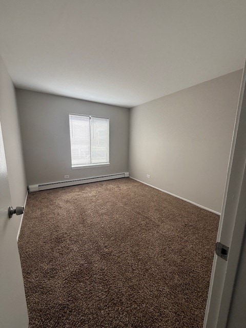 carpeted empty room featuring a baseboard heating unit and baseboards