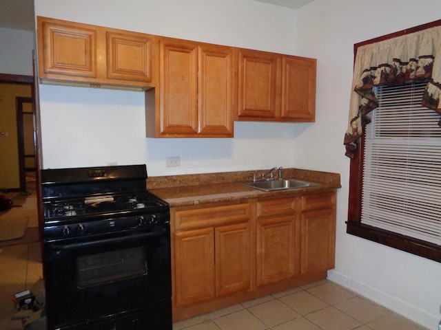 kitchen with light tile patterned floors, brown cabinetry, a sink, black range with gas cooktop, and dark countertops