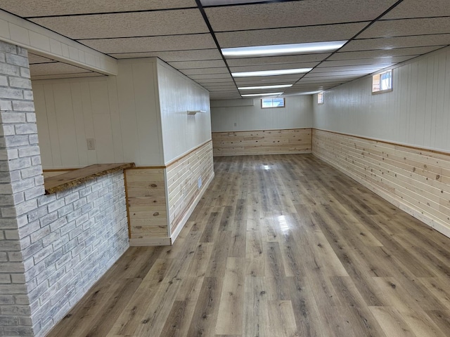 below grade area featuring a paneled ceiling, wood finished floors, and brick wall