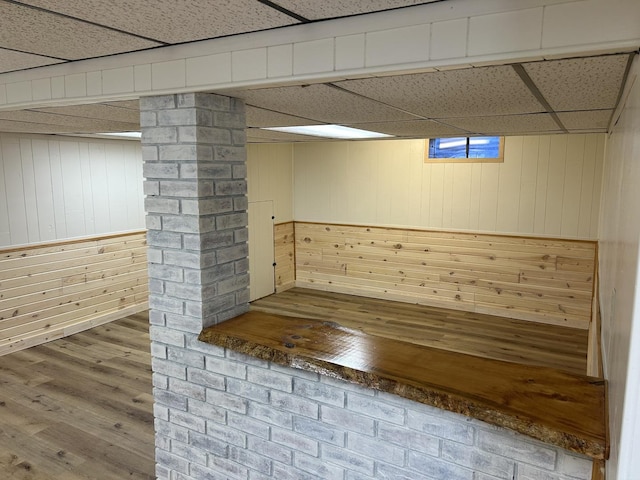 basement featuring wooden walls, a paneled ceiling, and wood finished floors