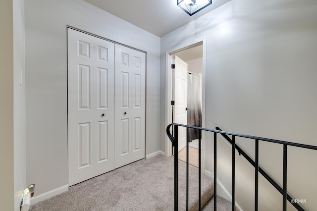 corridor featuring light carpet, an upstairs landing, and baseboards