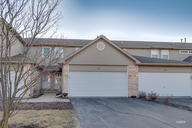 multi unit property featuring a garage, brick siding, roof with shingles, and driveway