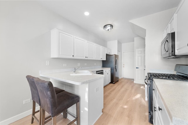 kitchen with a kitchen breakfast bar, a peninsula, white cabinets, stainless steel appliances, and a sink