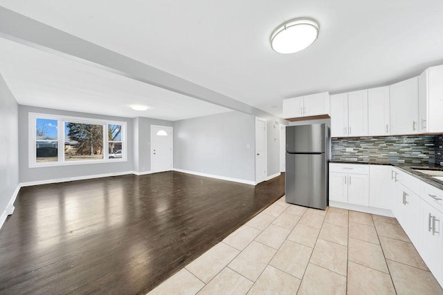 kitchen with dark countertops, open floor plan, decorative backsplash, freestanding refrigerator, and white cabinets