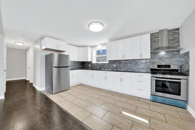 kitchen with a sink, appliances with stainless steel finishes, dark countertops, wall chimney range hood, and tasteful backsplash