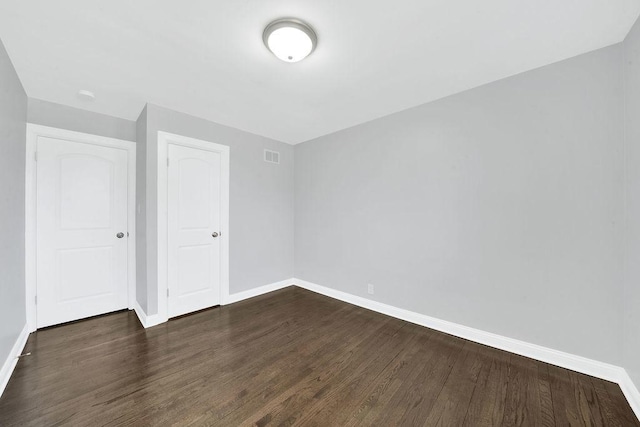 unfurnished bedroom with dark wood-style floors, visible vents, and baseboards