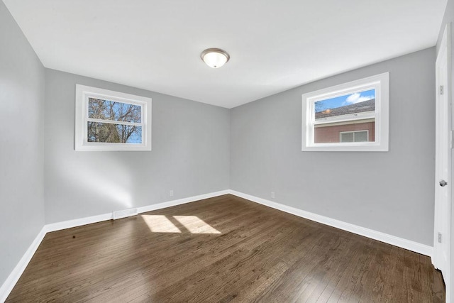 empty room with a wealth of natural light, baseboards, and dark wood-type flooring